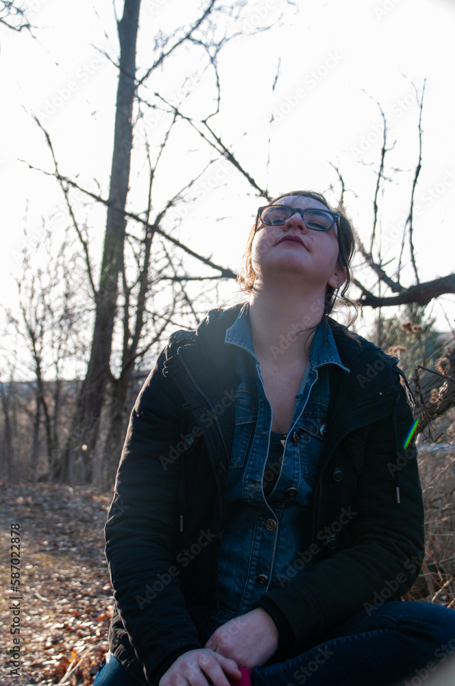 A woman sitting on a log backlit by the sun enjoys the weather in the forest A woman sitting on a log backlit by the sun enjoys the weather in the forest