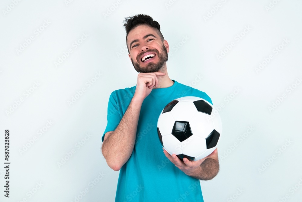 Optimistic Young man holding a ball over white background keeps hands partly crossed and hand under chin, looks at camera with pleasure. Optimistic Young man holding a ball over white background keeps hands partly crossed and hand under chin, looks at camera with pleasure.