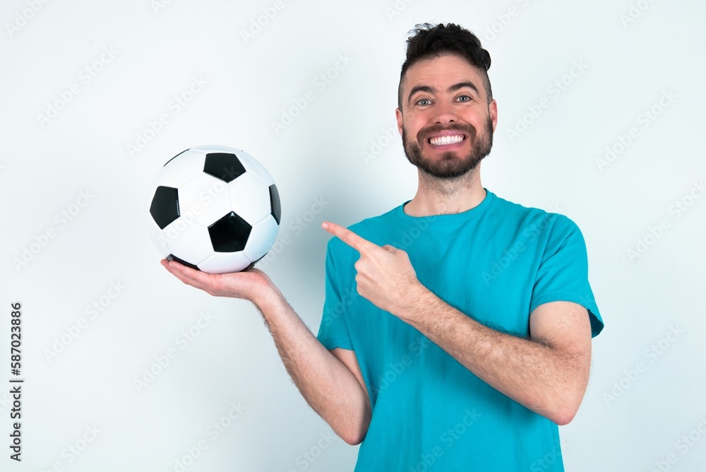 Young man holding a ball over white background pointing and holding hand showing adverts