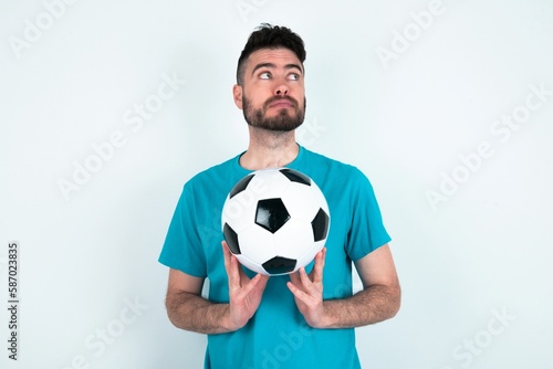 Charming cheerful Young man holding a ball over white background making up plan in mind holding hands together, setting up an idea.