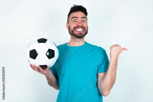 Lovely Young man holding a ball over white background pointing aside with forefinger, showing at copy space having news about bargains