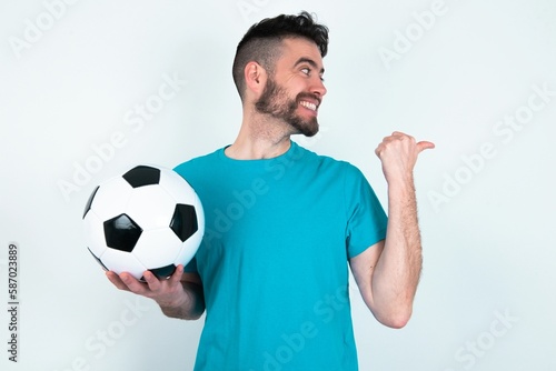 Charming Young man holding a ball over white background looking at copy space having advertisements