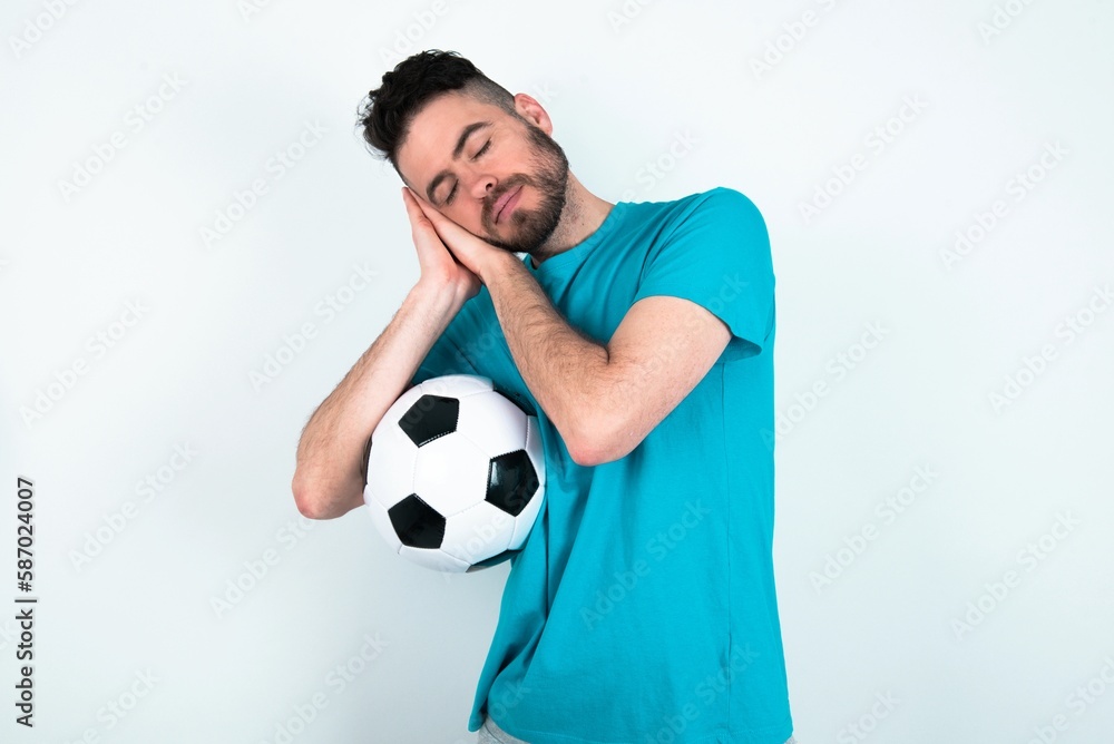 Young man holding a ball over white background sleeping tired dreaming and posing with hands together while smiling with closed eyes.