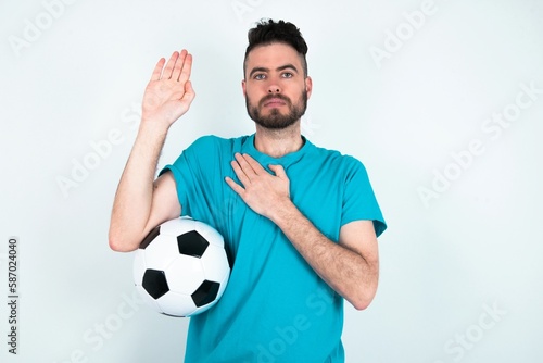 Young man holding a ball over white background Swearing with hand on chest and open palm, making a loyalty promise oath