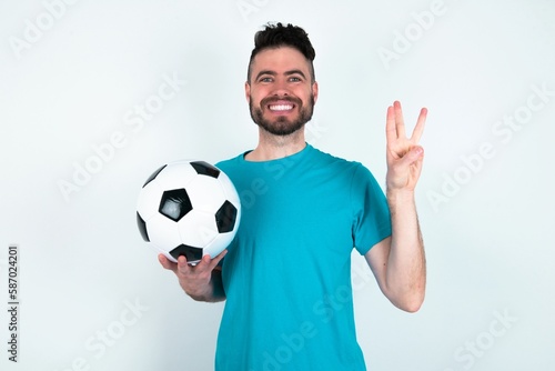 Young man holding a ball over white background showing and pointing up with fingers number three while smiling confident and happy.