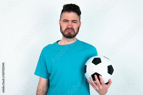 Displeased upset Young man holding a ball over white background frowns face as going to cry, being discontent and unhappy as can't achieve goals,  Disappointed model has troubles © Jihan