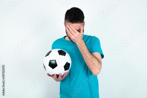 Fototapeta Naklejka Na Ścianę i Meble -  Young man holding a ball over white background covering her face with her hands, being devastated and crying. Sad concept
