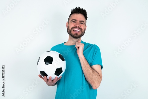 Positive Young man holding a ball over white background smiles happily, glad to receive pleasant news from interlocutor, keeps hands together. People emotions concept.