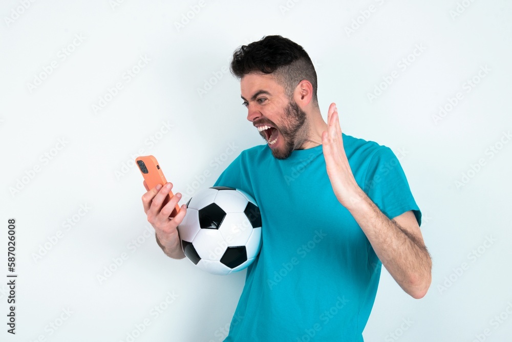 Angry Young man holding a ball over white background screaming on the phone, having an argument with an employee. Troubles at work.