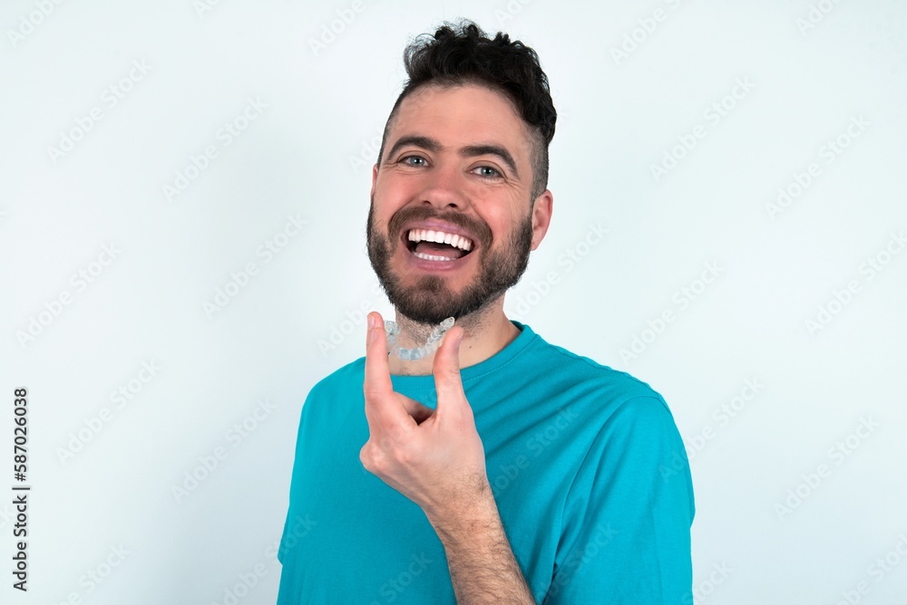 Young man over white background holding an invisible aligner ready to use it. Dental healthcare and confidence concept. Young man over white background holding an invisible aligner ready to use it. Dental healthcare and confidence concept.