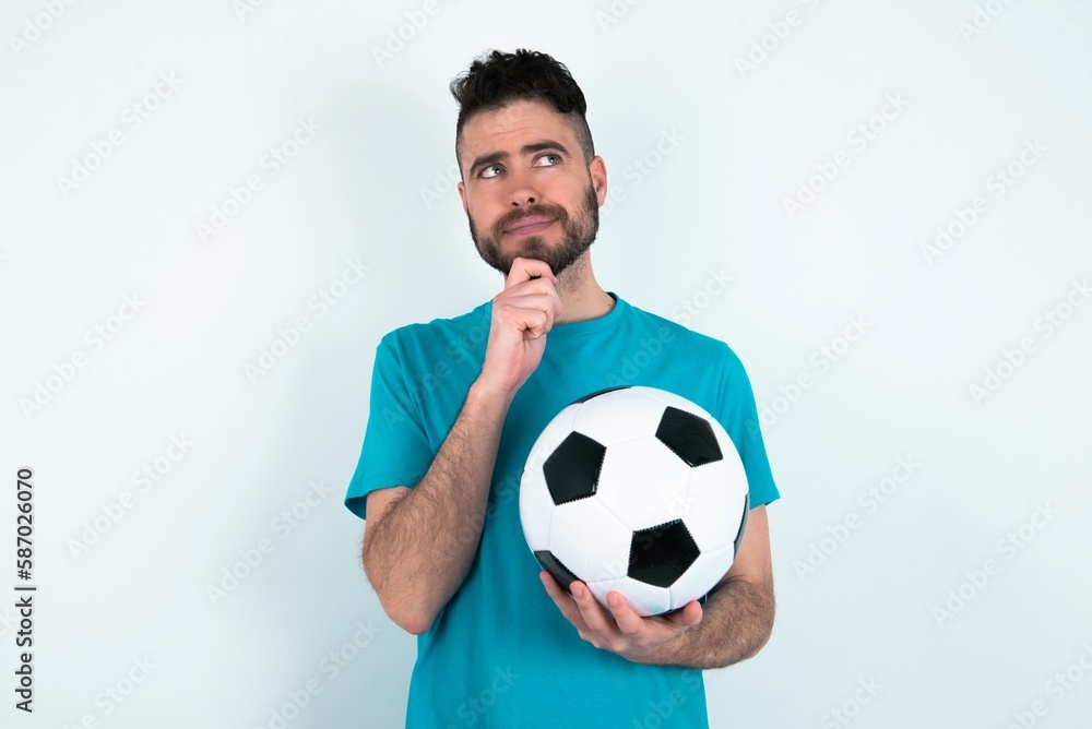 Thoughtful Young man holding a ball over white background holds chin and looks away pensively makes up great plan Thoughtful Young man holding a ball over white background holds chin and looks away pensively makes up great plan