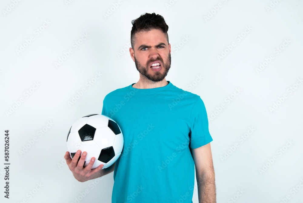 Portrait of dissatisfied Young man holding a ball over white background smirks face, purses lips and looks with annoyance at camera, discontent hearing something unpleasant Portrait of dissatisfied Young man holding a ball over white background smirks face, purses lips and looks with annoyance at camera, discontent hearing something unpleasant