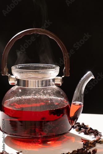 Red hibiscus tea from the petals of a Sudanese rose in a glass teapot, steam from a teapot on a black background