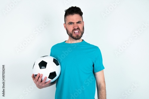 Portrait of dissatisfied Young man holding a ball over white background smirks face, purses lips and looks with annoyance at camera, discontent hearing something unpleasant