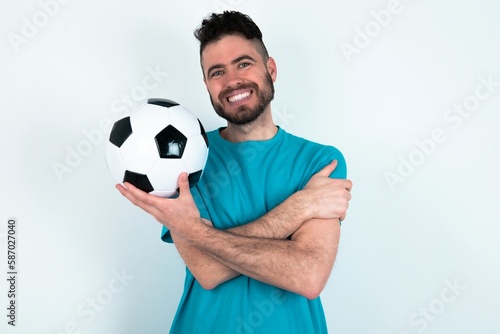 Charming pleased Young man holding a ball over white background embraces own body, pleasantly feels comfortable poses. Tenderness and self esteem concept