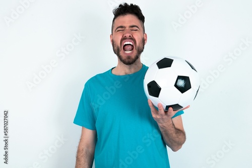 Young man holding a ball over white background yawns with opened mouth stands. Daily morning routine