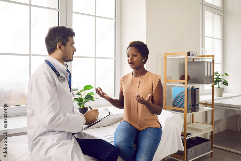 Female patient talking to doctor in his office. Worried young black ...
