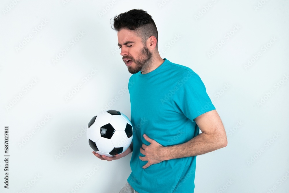 Young man holding a ball over white background got stomachache