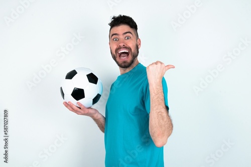 Impressed Young man holding a ball over white background point back empty space © Jihan