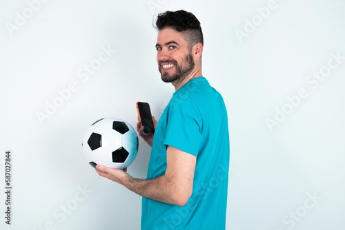 Rear view photo portrait of Young man holding a ball over white background using smartphone smiling