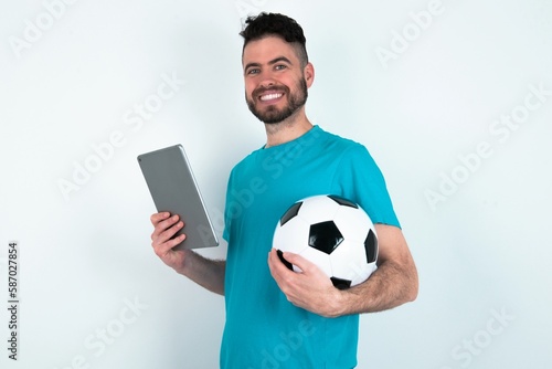 Photo of optimistic Young man holding a ball over white background hold tablet