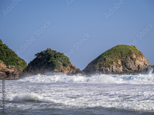 Beach, waves, and hills covered with jungle in the background