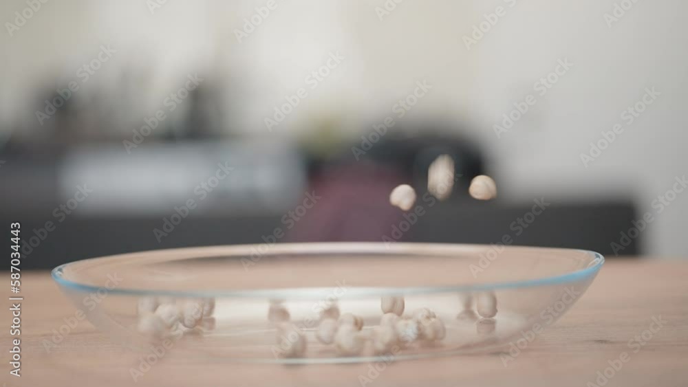 Dry chickpeas pour into a plate and jump out of it on a wooden table. Slow motion. Dry chickpeas pour into a plate and jump out of it on a wooden table. Slow motion.