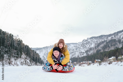 Couple having fun on winter vacation, tube in snow, while spending time outdoors on snowy winter day in mountains