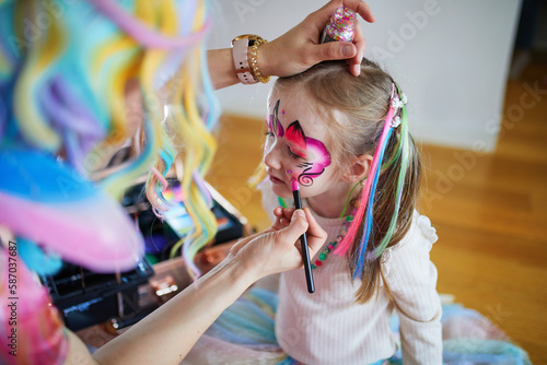 Artist painting little preschooler girl like unicorn on a birthday party photo