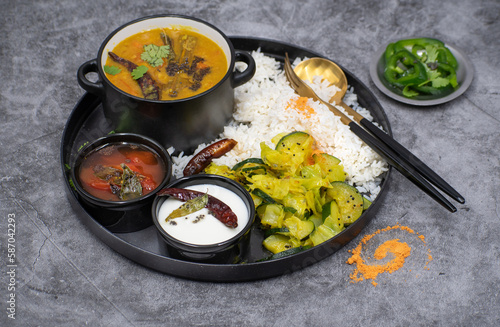 Indian vegan dishes on platter consisting of rice, sambar, rasam, squash curry, gray plate