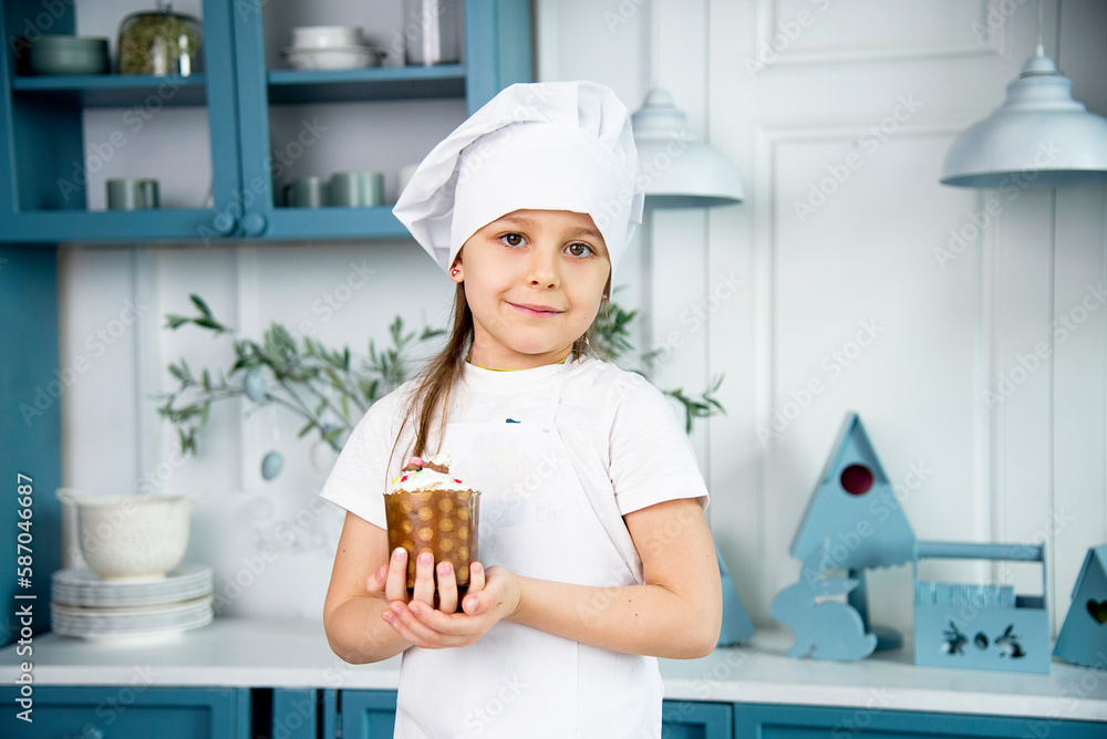 little cute funny smiling girl wearing a white chef's hat and uniform holding decorating easter cake in the blue and white kitchen with easter decoration little cute funny smiling girl wearing a white chef's hat and uniform holding decorating easter cake in the blue and white kitchen with easter decoration