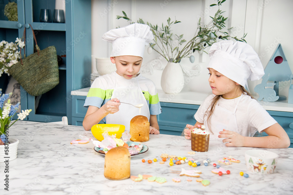 two little cute funny smiling kids wearing a white chef's hats and uniform decorating easter bread with food coloring in the blue and white kitchen with easter decorations two little cute funny smiling kids wearing a white chef's hats and uniform decorating easter bread with food coloring in the blue and white kitchen with easter decorations