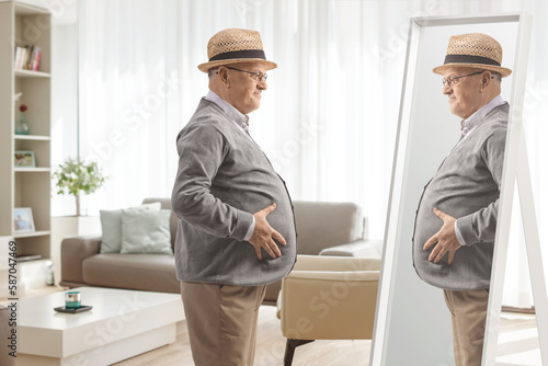 Elderly man with a big belly looking at a mirror at home