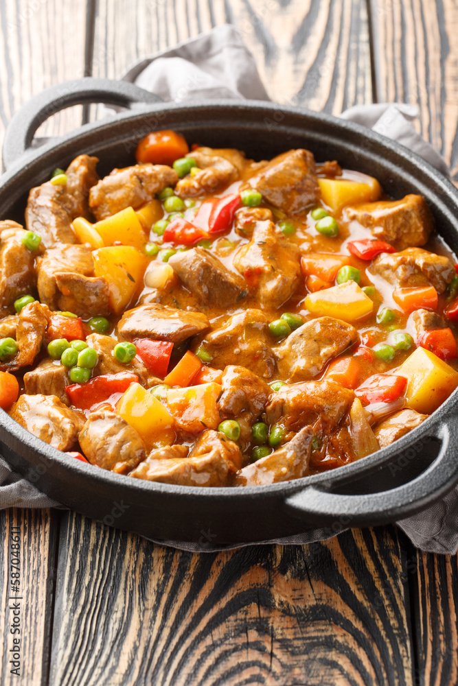 Veal stew with vegetables potatoes, carrots, green peas, onions and spices close-up in a frying pan on a wooden table. Vertical Veal stew with vegetables potatoes, carrots, green peas, onions and spices close-up in a frying pan on a wooden table. Vertical