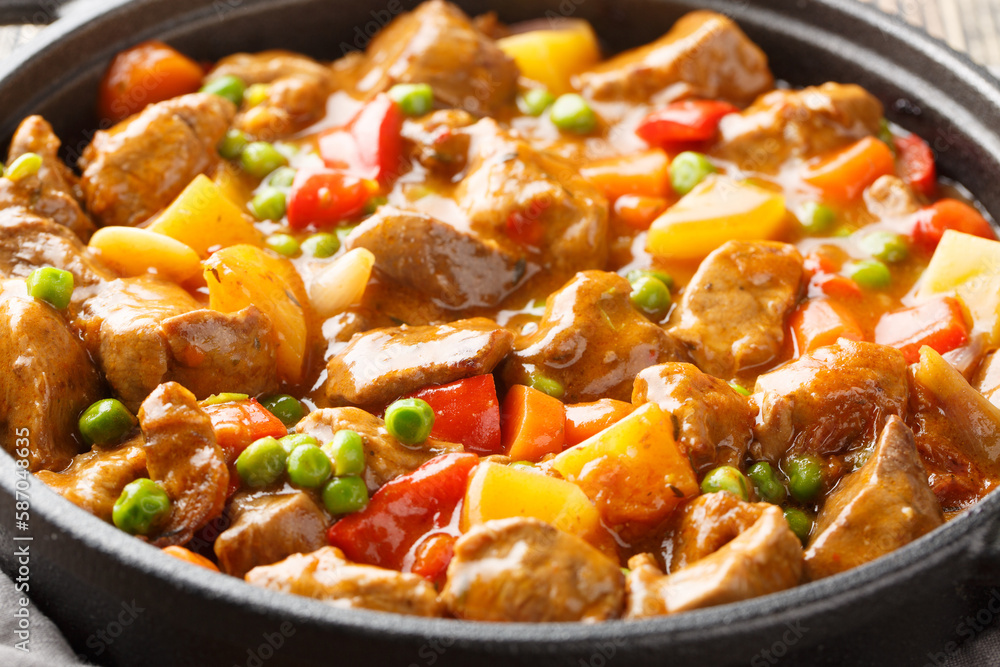 Slow cooked beef with potatoes, carrots, tomatoes, green peas, onions and spices close-up in a frying pan on a wooden table. Horizontal
