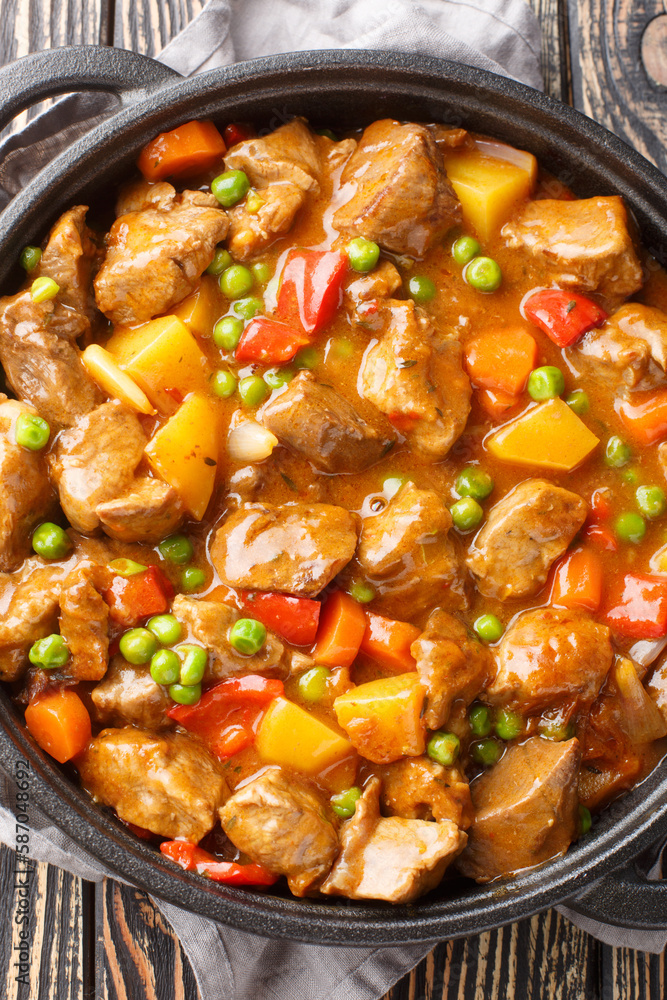 Beef stew with potatoes, carrots, green peas and spices close-up in a frying pan on a wooden table. Vertical Beef stew with potatoes, carrots, green peas and spices close-up in a frying pan on a wooden table. Vertical