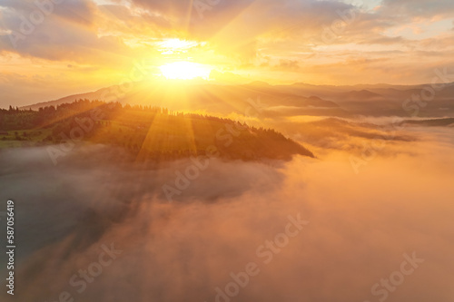 Mountains in clouds at sunrise in summer. Aerial view of mountain peak with green trees in fog. Beautiful landscape with high rocks, forest, sky. © Ryzhkov Oleksandr