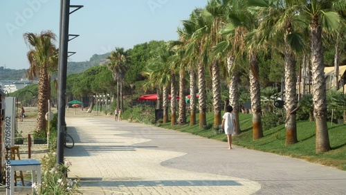 Durres, Albania - 15 September, 2020: Woman with white dress walking among palm trees on promenade on summer vacation photo