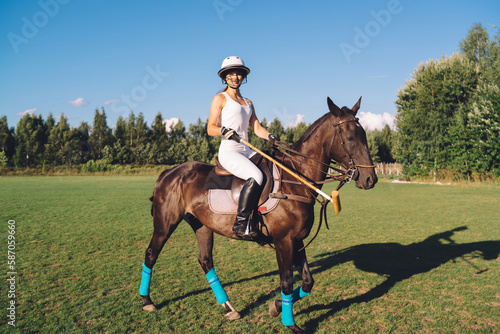 Graceful female polo player riding horse on field under blue sky