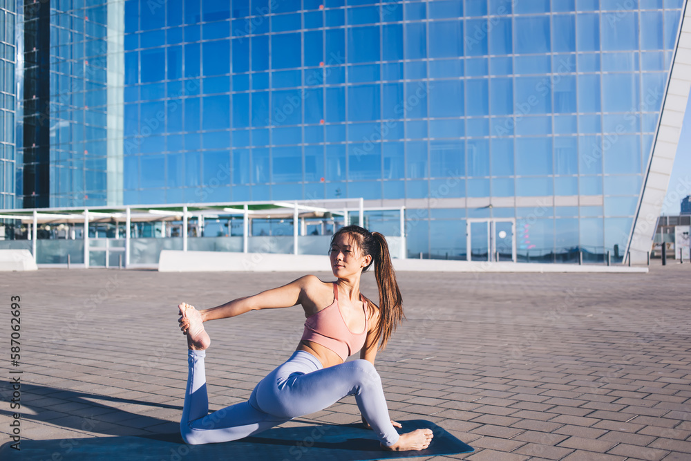 Good looking flexible woman with slim body doing asana pose during morning workout at urban setting, female trainer enjoying active healthy lifestyle practicing hatha yoga reaching body positive