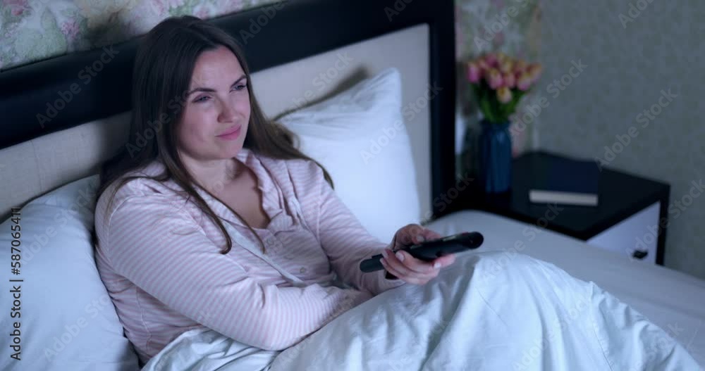 The girl lying on the bed switches channels using the remote control. The girl lying on the bed switches channels using the remote control.