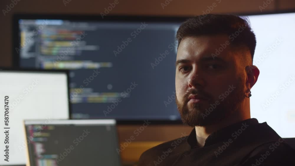 Portrait shooting of a young IT specialist. A web developer is sitting in his office in front of multiple monitors. Portrait shooting of a young IT specialist. A web developer is sitting in his office in front of multiple monitors.
