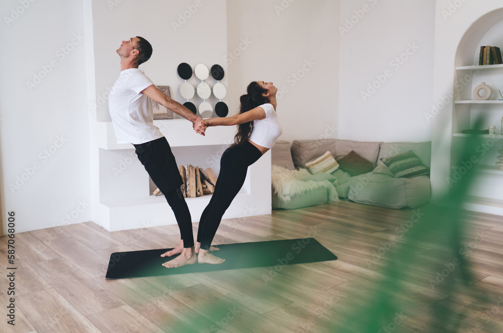 Obraz premium Flexible couple stretching in yoga pose in living room