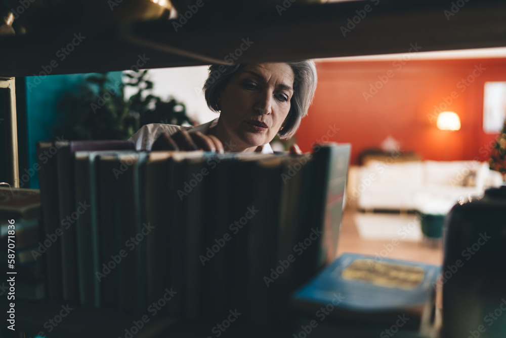 Focused mature woman searching books row in shelf