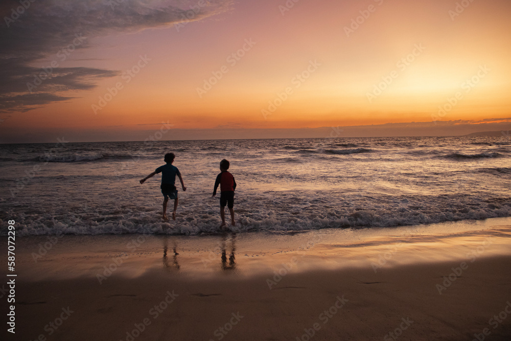 Niños felices jugando y brincando en la playa durante la puesta de sol en Puerto Vallarta México
