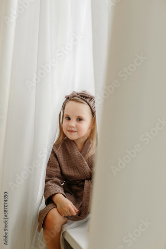 A girl in a brown robe is sitting on the windowsill, smiling