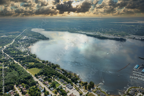 This breathtaking drone photo captures the stunning beauty of Lake Simcoe at sunset from Barrie Lakeshore Centennial Park. The sky is filled with a dramatic display of fluffy, billowy clouds, adding d