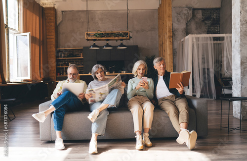 Elderly group of friends relaxing on couch using gadgets and reading