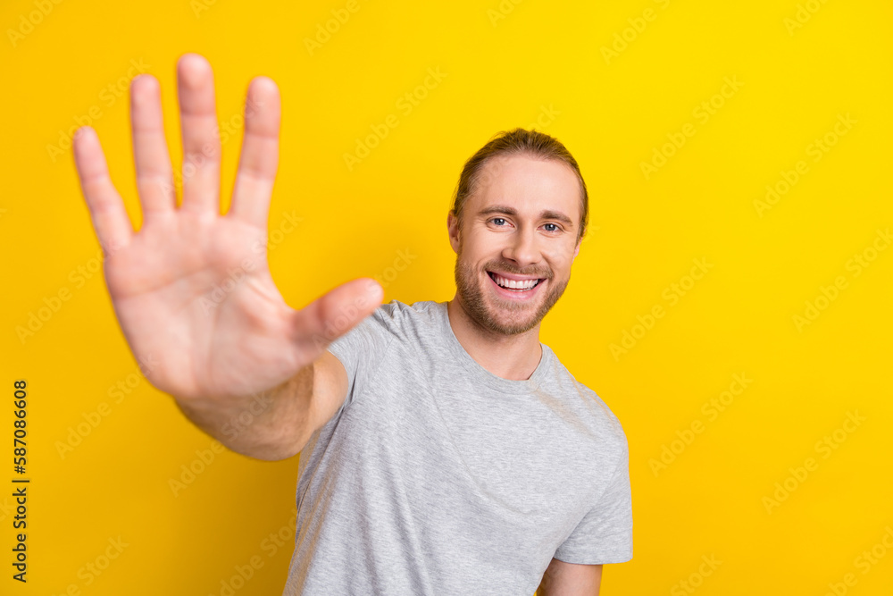 Photo of toothy beaming pleasant man with long hairstyle wear gray t-shirt showing palm at camera isolated on yellow color background Photo of toothy beaming pleasant man with long hairstyle wear gray t-shirt showing palm at camera isolated on yellow color background