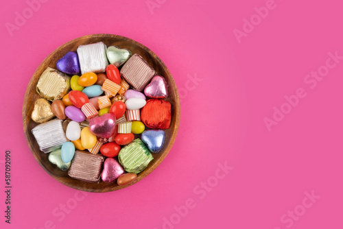 Bowl of candies  top view photo of bowl of candies. Colorful sweets in the wooden plate. Isolated pink background  copy space for greetings. Wrapped luxury chocolate. Ramadan feast celebration concept